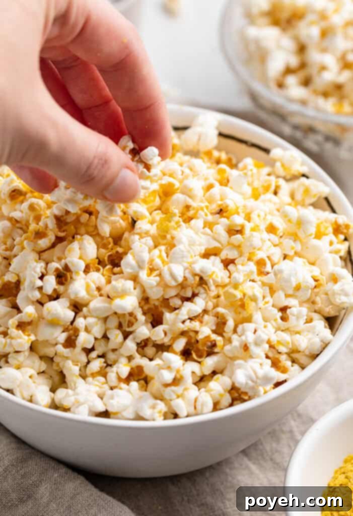 A hand reaching into a large bowl of freshly made, golden buttery vegan popcorn, highlighting its fluffy texture.