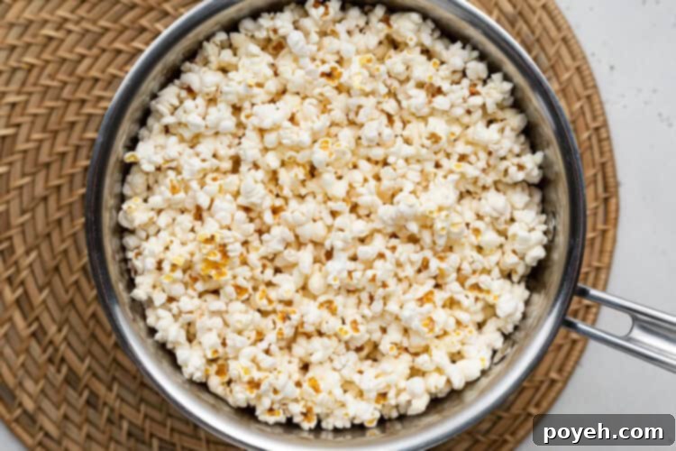 Overhead view of vegan popped popcorn filling a large silver pot, still on the stove with a wicker placemat nearby.