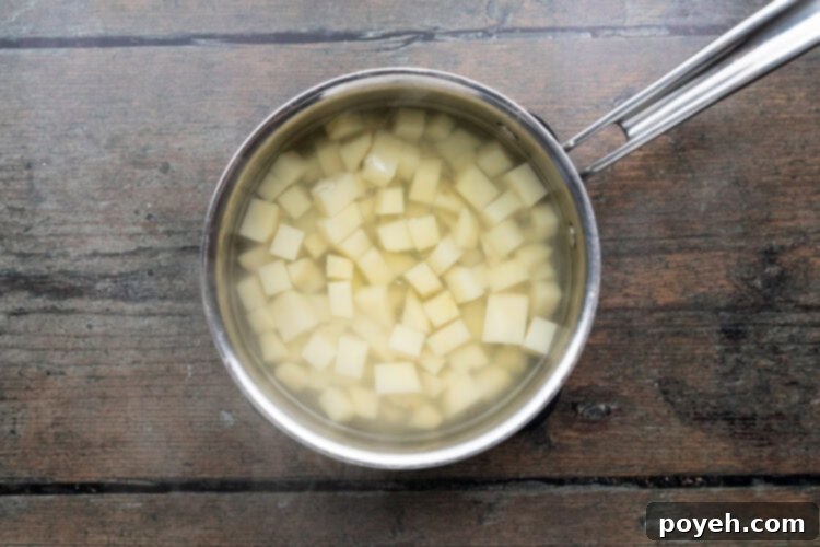 Overhead view of a small saucepan with boiled, cubed potatoes on a wooden table.