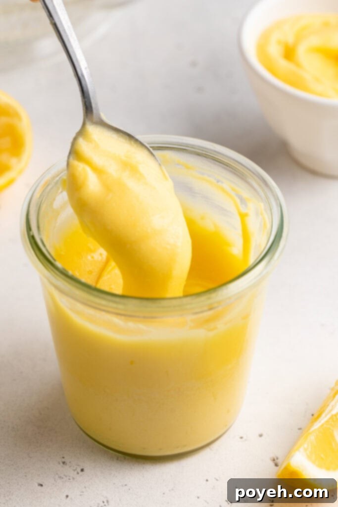 3/4-angle view of a small glass of keto lemon curd, with a silver spoon lifting lemon curd out of the glass.