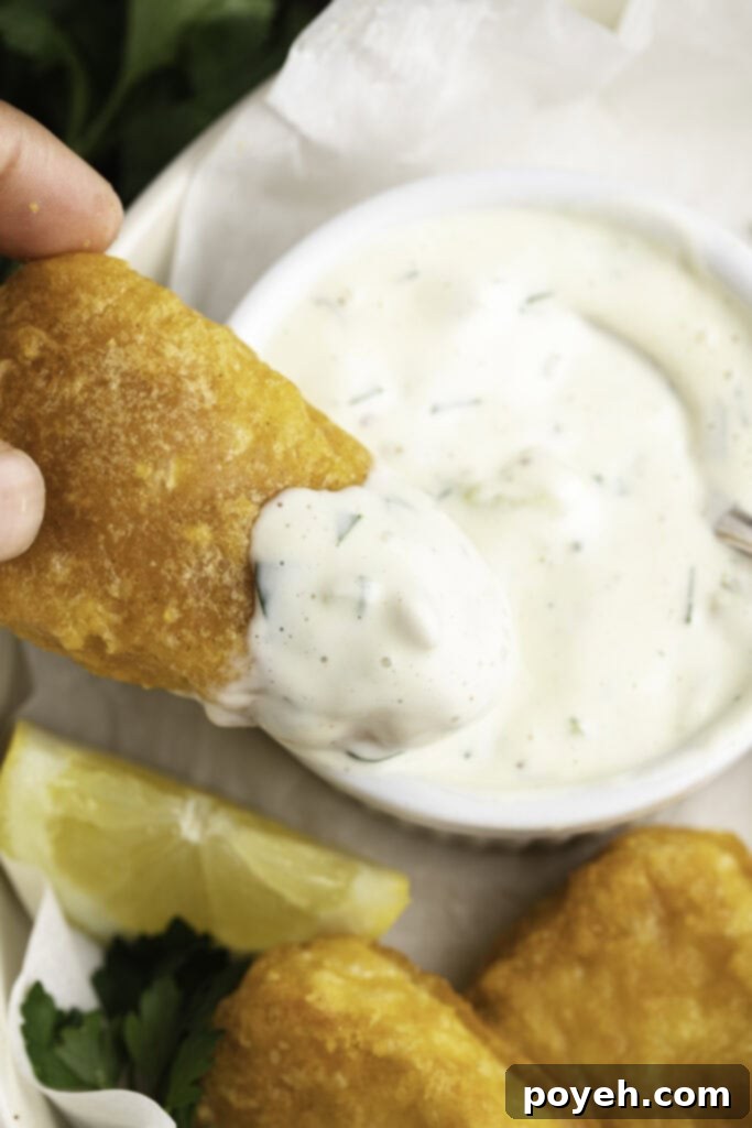 Vegan tartar sauce generously drizzled on a piece of vegan breaded and fried fish, ready to be eaten.