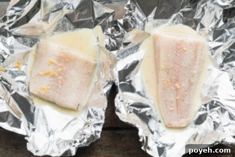 Overhead view of two cod fillets in foil packets with lemon-butter sauce.