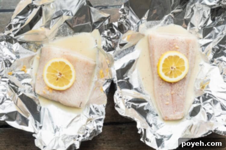Overhead view of two cod fillets in foil packets with lemon-butter sauce and lemon coins.