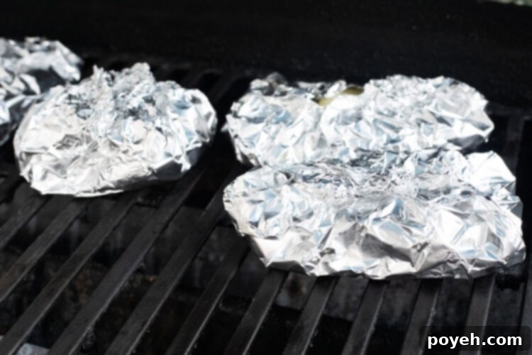 Cod fillets wrapped tightly in aluminum foil packets on a grill over indirect heat.