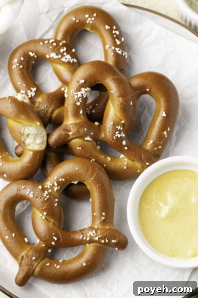 Four salted twisted soft pretzels artfully arranged on a white plate, accompanied by a small ramekin of golden cheese sauce.