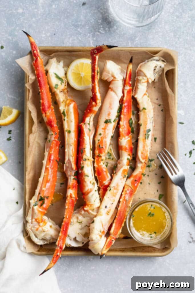 Overhead view of grilled crab legs lined up on a baking sheet lined with parchment paper, next to a small bowl of butter sauce.