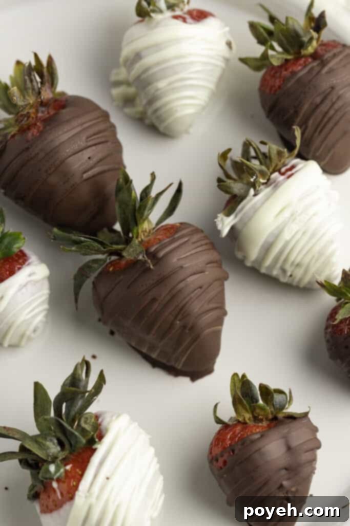 Close up photo of dark chocolate and white chocolate covered strawberries on a white plate, showcasing the glossy chocolate coating and vibrant red fruit.