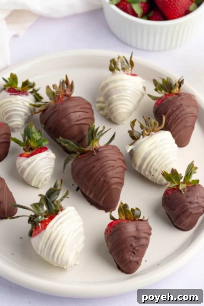Dark chocolate and white chocolate covered strawberries on a white plate on a white background, ready to be enjoyed.
