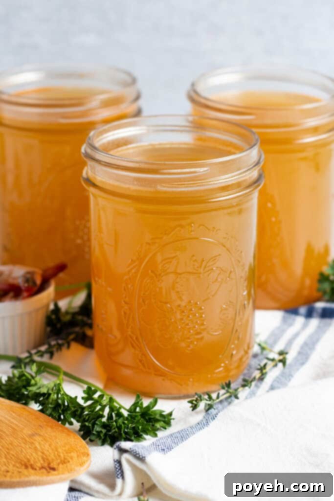 Savory Shrimp Stock from Scratch 2 Side, angled view of 3 mason jars of shrimp stock on a title surrounded by fresh herbs and a dish towel.