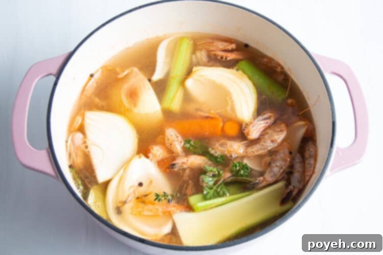 Savory Shrimp Stock from Scratch 8 Overhead view of shrimp stock ingredients and water in large dutch oven on neutral background.
