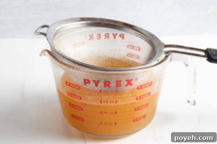 Savory Shrimp Stock from Scratch 9 Sieve resting in glass measuring cup containing strained shrimp stock without aromatics.