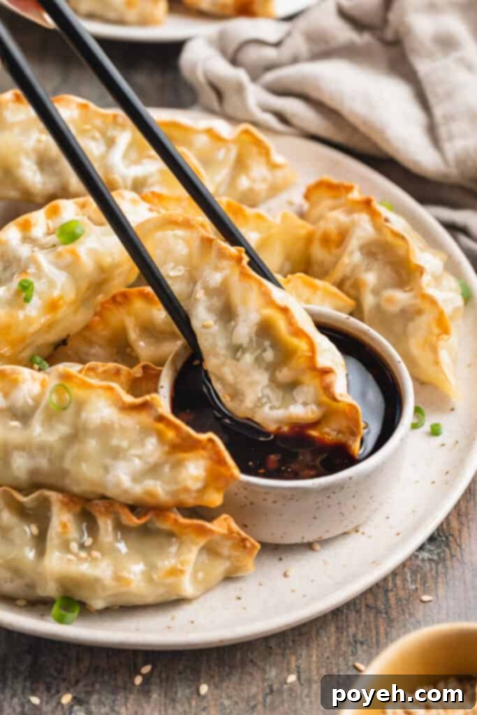 Crispy air fryer dumplings on plate, with one dumpling being held by chopsticks and dipped into a small ramekin of soy sauce.