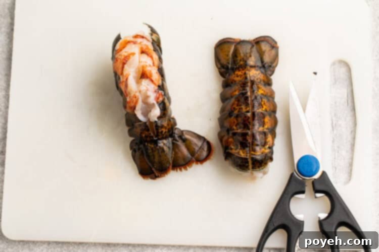 Overhead view of 2 lobster tails on a white cutting board, showing how to pull lobster meat out of one tail.