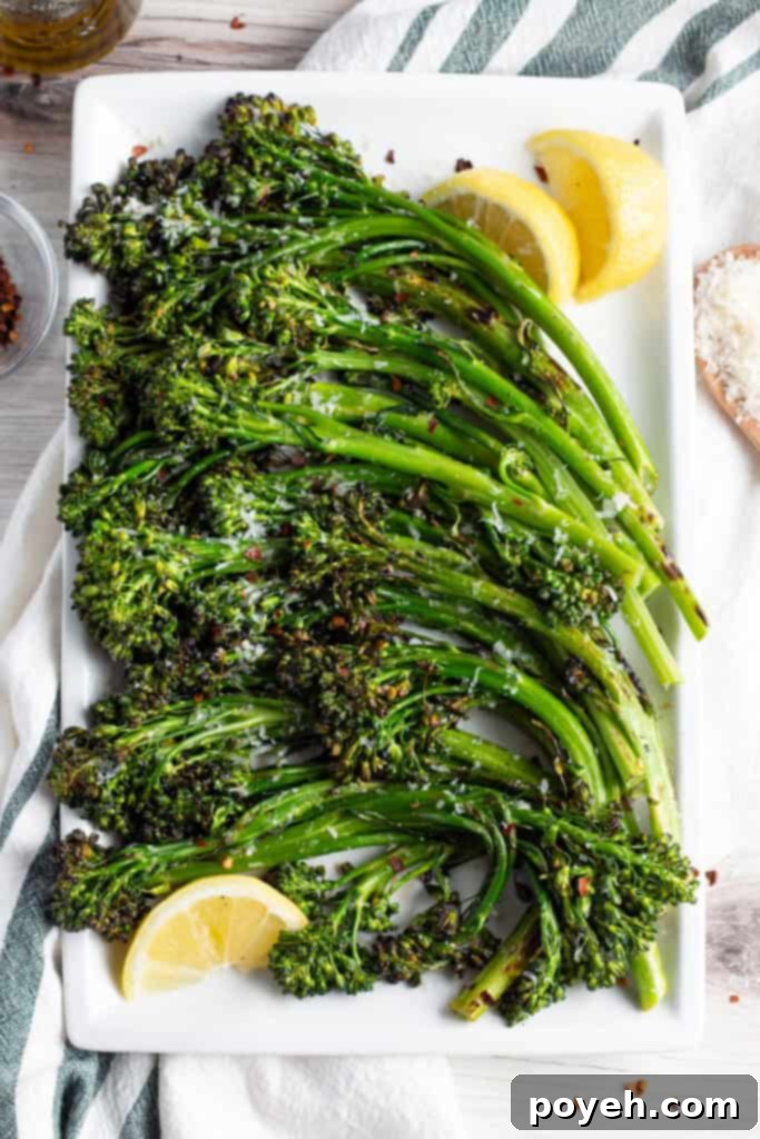 Overhead view of tender, grilled broccolini topped with parmesan and red pepper flakes on a cutting board with lemon wedges.