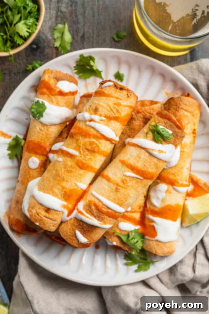 Overhead view of perfectly golden-brown air fryer flautas garnished with sour cream and hot sauce, served on a clean white paper plate.