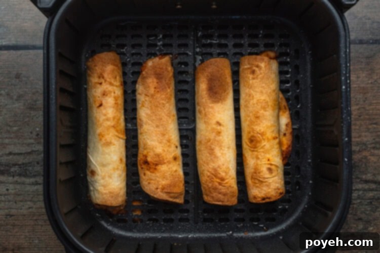 Overhead view of four golden brown and perfectly crispy air fryer flautas arranged in an air fryer basket after cooking.
