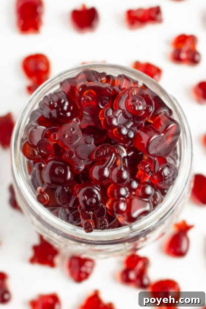 Sour Cherry Chews 5 Close-up, overhead view of a glass jar overflowing with bright red gummies on a white countertop.