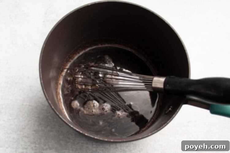 Sour Cherry Chews 8 Overhead view of a black saucepan with tart cherry juice, lemon juice, lime juice, honey, and a whisk on a white countertop.