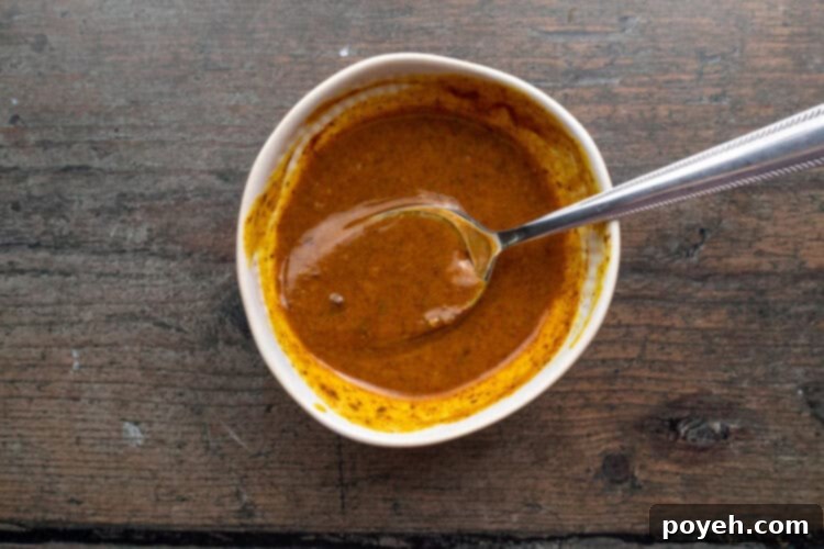 Overhead view of smoky mustard sauce in a small white bowl with a silver spoon.
