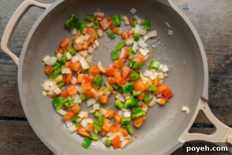 Overhead view of a large skillet filled with a colorful mix of sautéed onions, vibrant green bell peppers, and diced Roma tomatoes, perfectly cooked and ready for the omelette.
