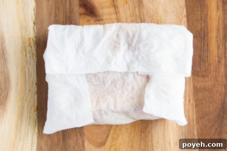 Overhead view of a toasted grilled cheese sandwich wrapped in a damp paper towel on a wooden cutting board.
