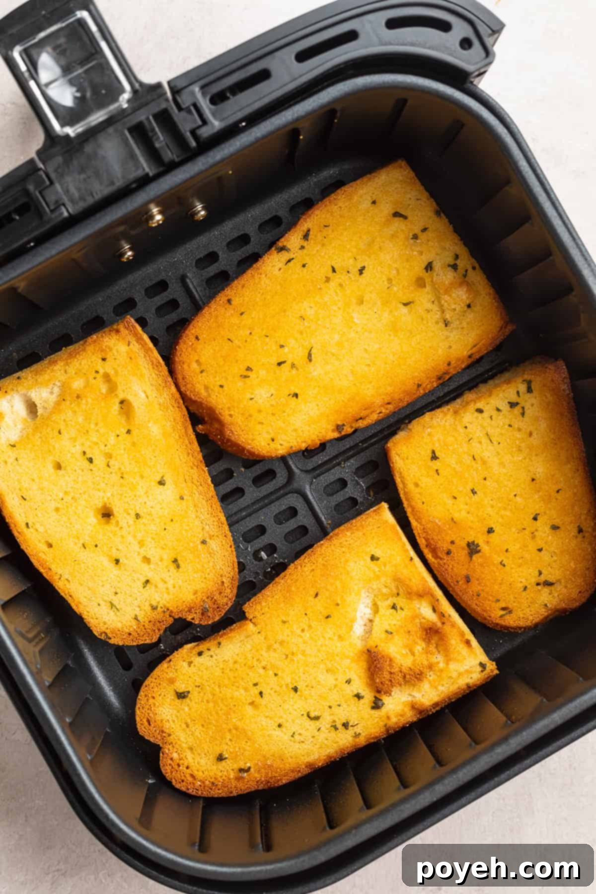 Overhead view of 4 pieces of garlic Texas toast in an air fryer basket on a white countertop.