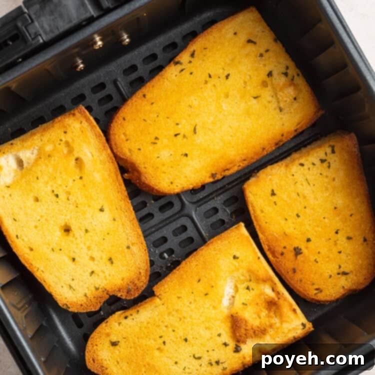 Overhead view of 4 pieces of garlic Texas toast in an air fryer basket on a white countertop.