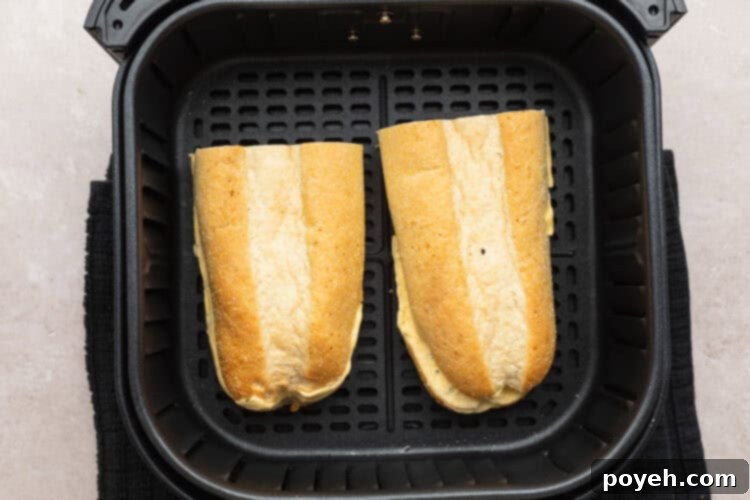 Overhead view of two halves of a frozen garlic bread loaf in an air fryer basket, before air frying.