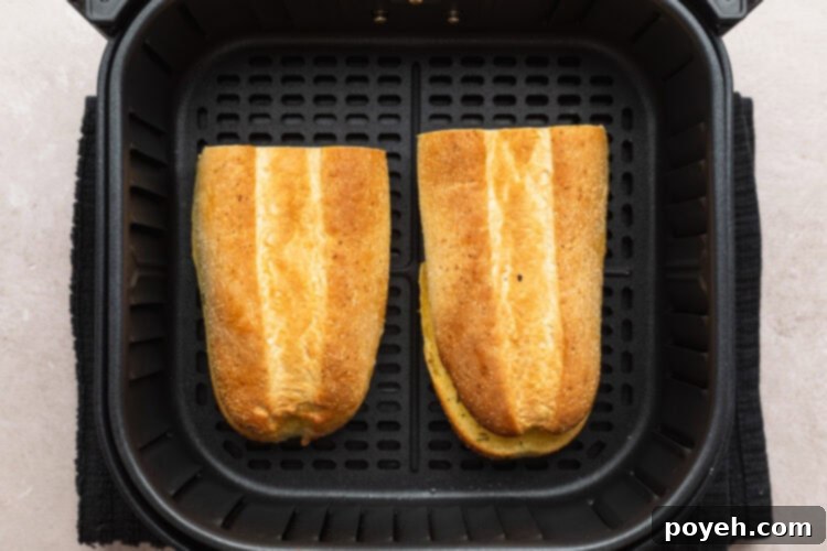 Overhead view of two halves of a frozen garlic bread loaf in an air fryer basket, after air frying.