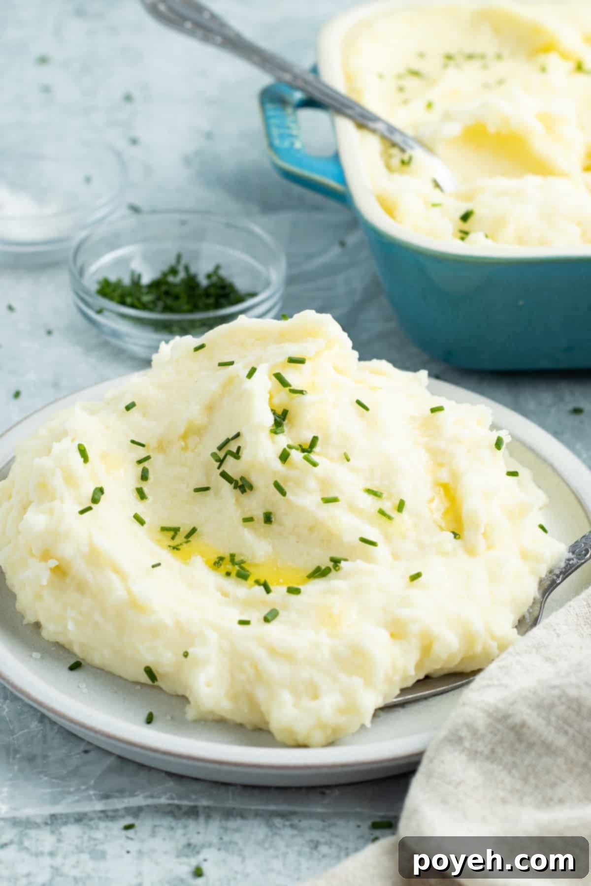 Side view of a bowl of fluffy potato mousseline in front of a casserole dish of potato mousseline.