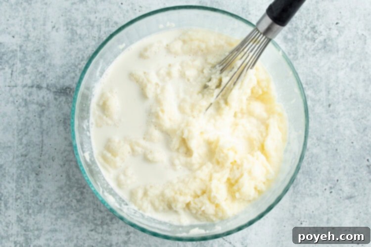 Overhead view of milk and cream added to a bowl of riced potatoes and then whisked until fluffy.