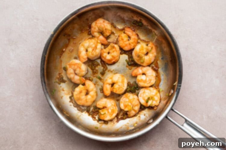 Overhead view of sautéed shrimp and diced green onion in a large silver skillet on a neutral countertop.
