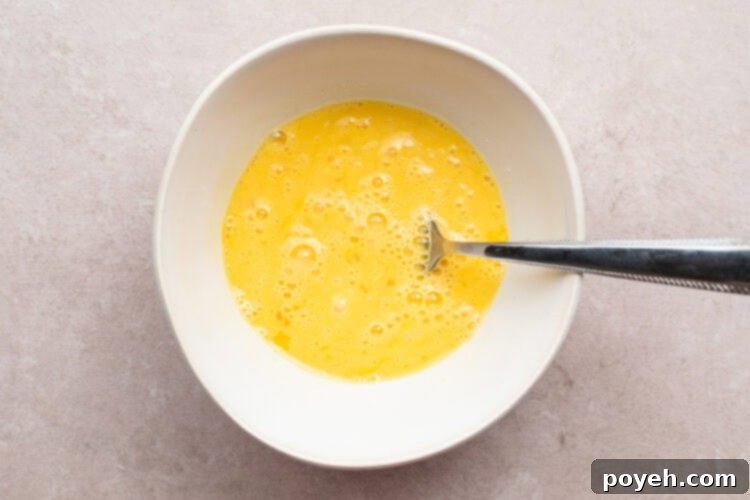 Overhead view of eggs and milk mixed together in a white bowl until egg mixture is pale yellow.