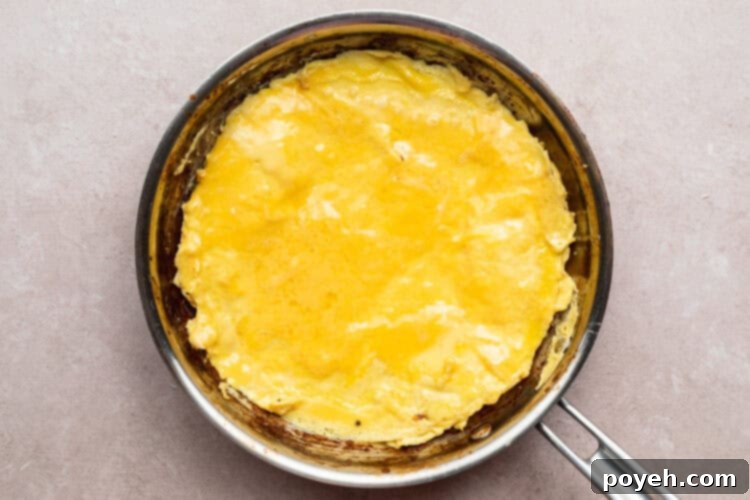 Overhead view of firm, cooked eggs in a large silver skillet on a neutral countertop.