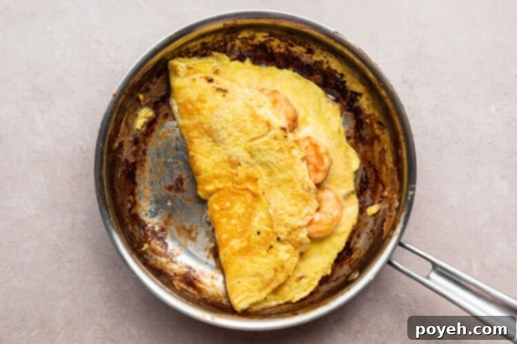 Overhead view of a folded shrimp omelette with green onions and eggs in a large silver skillet.