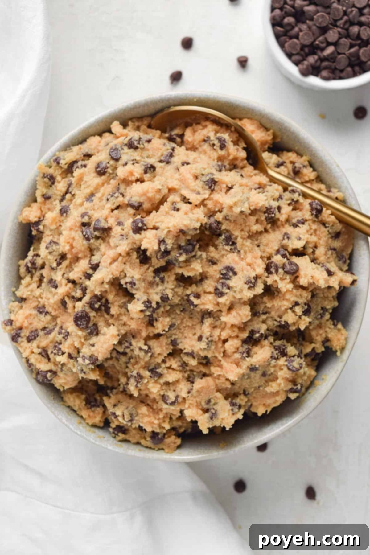 Overhead view of a bowl of keto cookie dough with a gold spoon on a white tabletop.