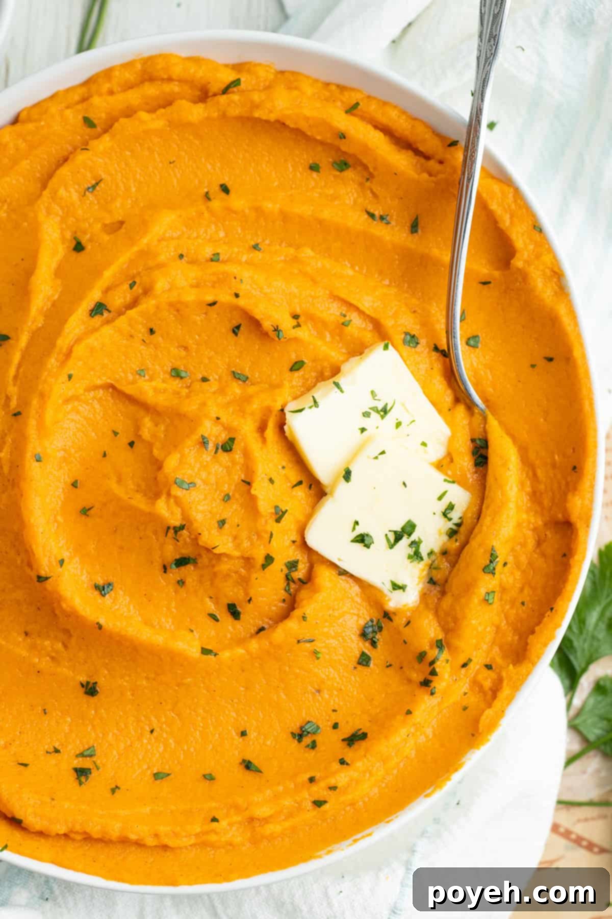 Overhead view of a bowl of whipped sweet potatoes with 2 pats of butter and fresh chives.