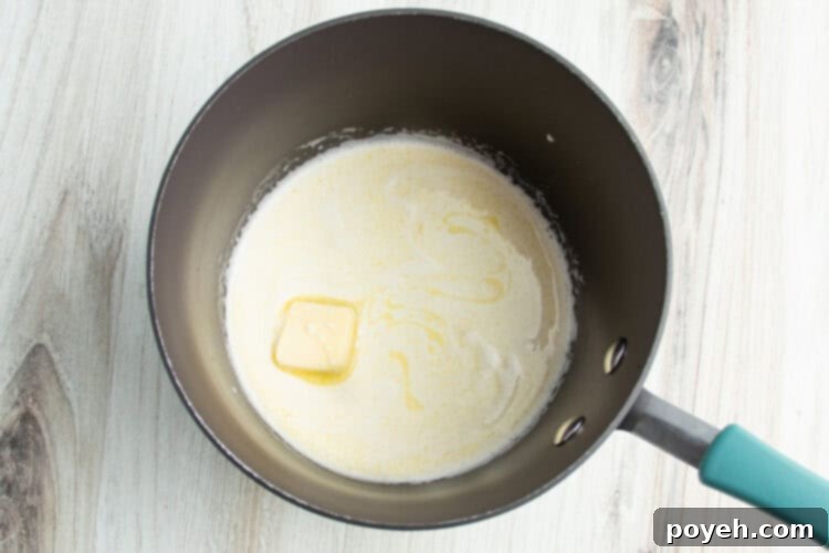 Overhead view of melting butter and heavy cream in a small saucepan on a white countertop.