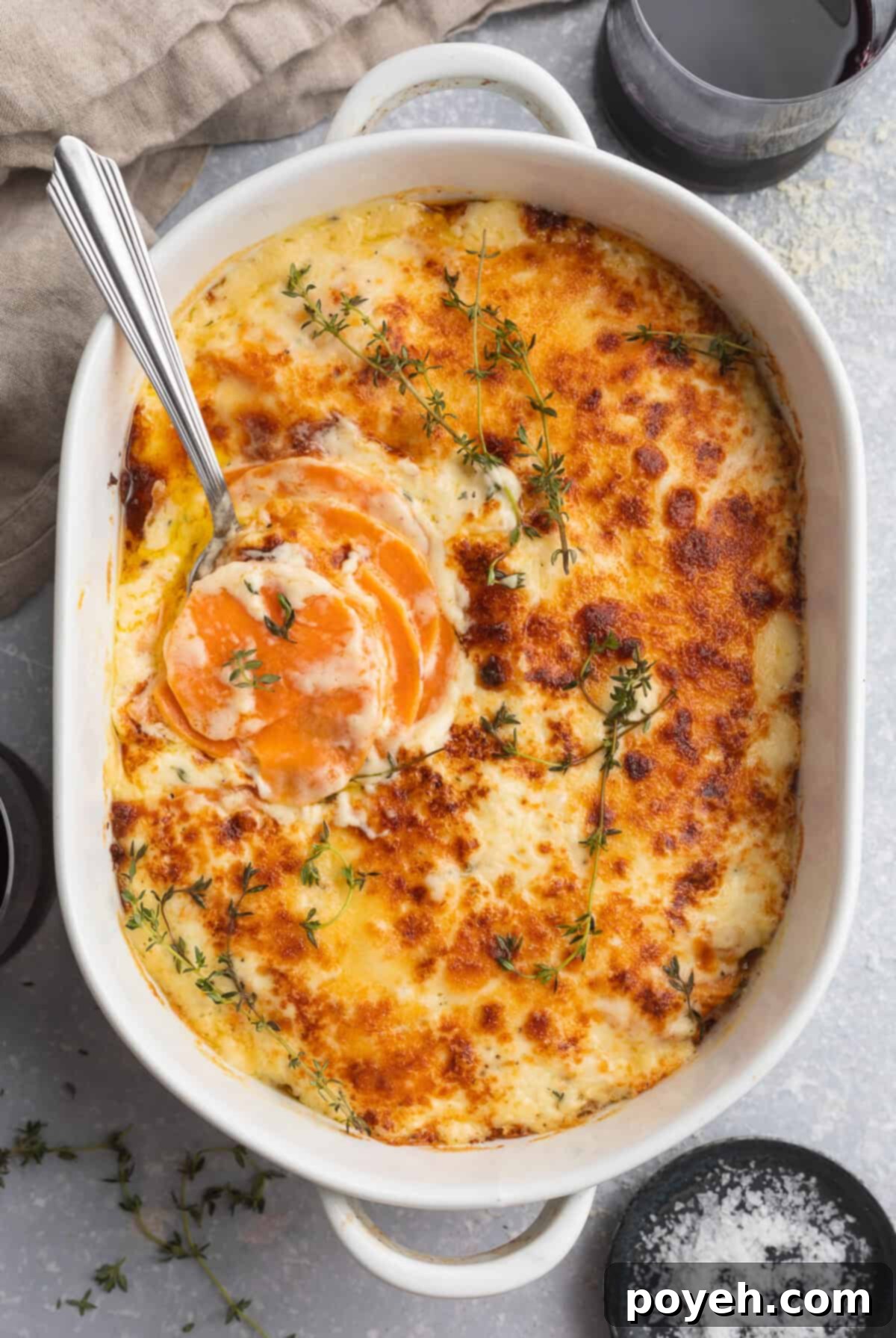 Overhead view of a large, oval casserole dish containing melty, cheesy, browned scalloped sweet potaotes.