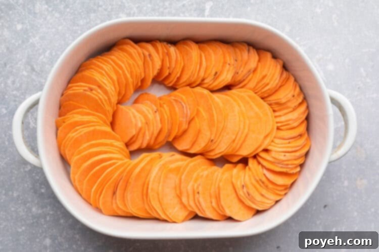 Overhead view of sweet potato slices arranged in a ring around the inside edge of an oval baking dish, with a row of slices in the center.