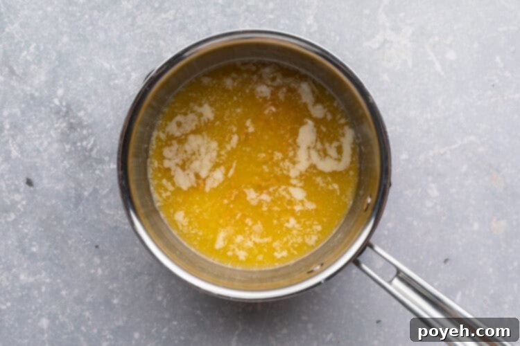 Overhead view of melted butter in a small saucepan on a neutral blue-gray background.
