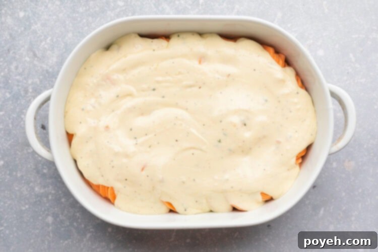 Overhead view of thinly sliced sweet potatoes covered with a creamy herb sauce in a large oval casserole dish.