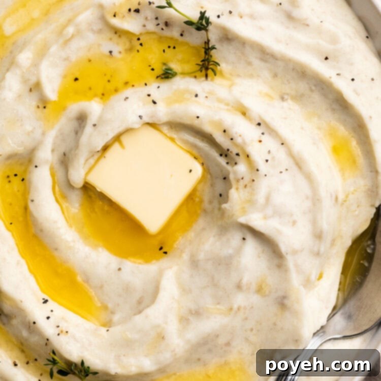 Velvety Whipped Potatoes 4 Close-up, overhead view of a large bowl of creamy whipped potatoes, swirled with melted butter and topped with a pat of butter and fresh herbs for garnish.