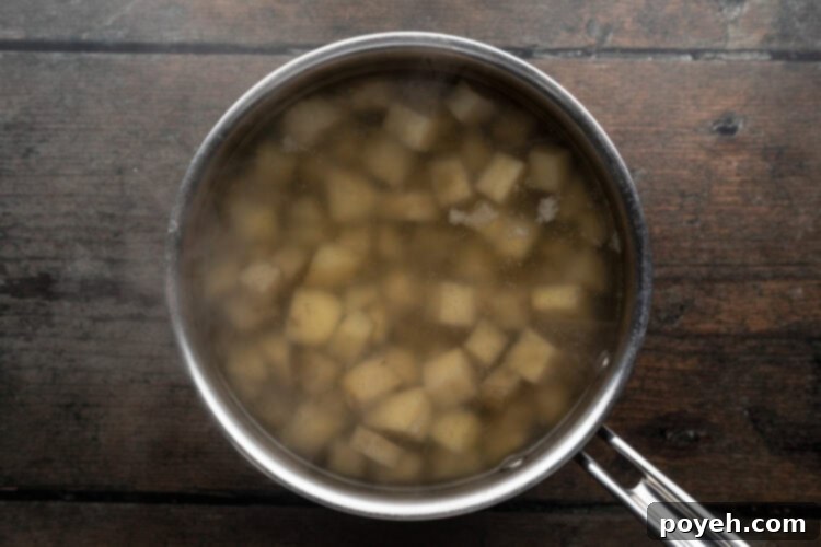 Velvety Whipped Potatoes 6 Overhead view of large silver pot holding cubed potatoes and cold salted water sitting on a wooden tabletop, ready for boiling.