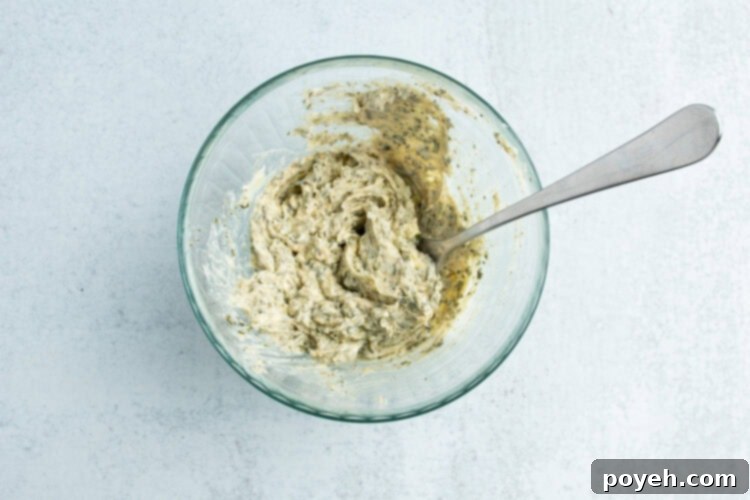 Overhead view of a small glass mixing bowl holding a compound butter mixture of garlic and fresh herbs.