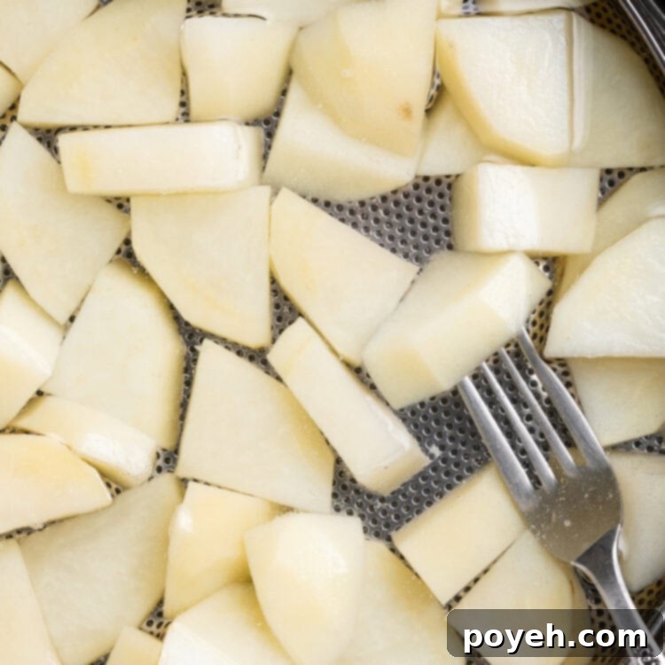 Overhead close-up view of blanched potatoes in a saucepan with a strainer.