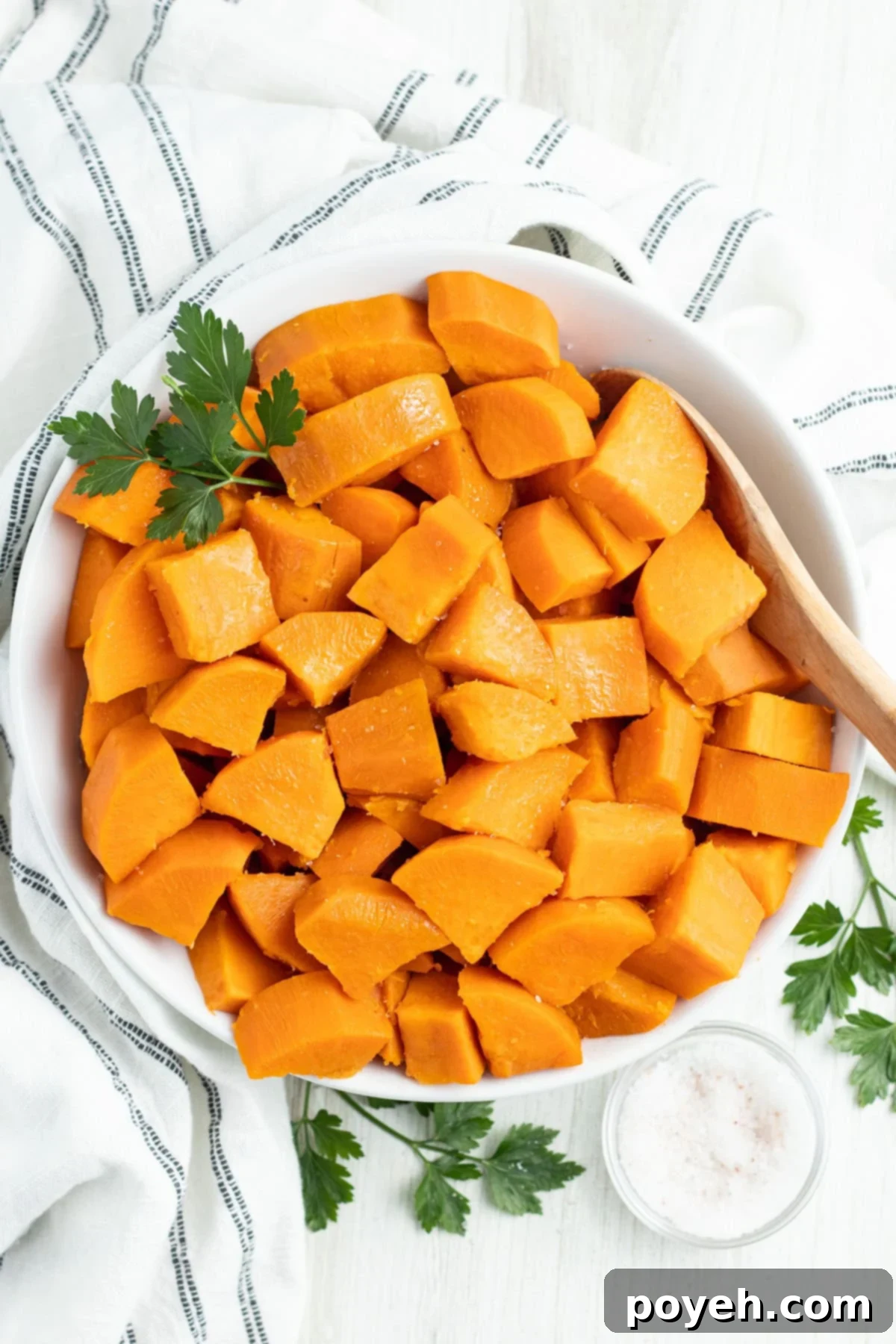 Overhead view of a large white bowl of cubed, boiled sweet potatoes on a table with a white tablecloth.