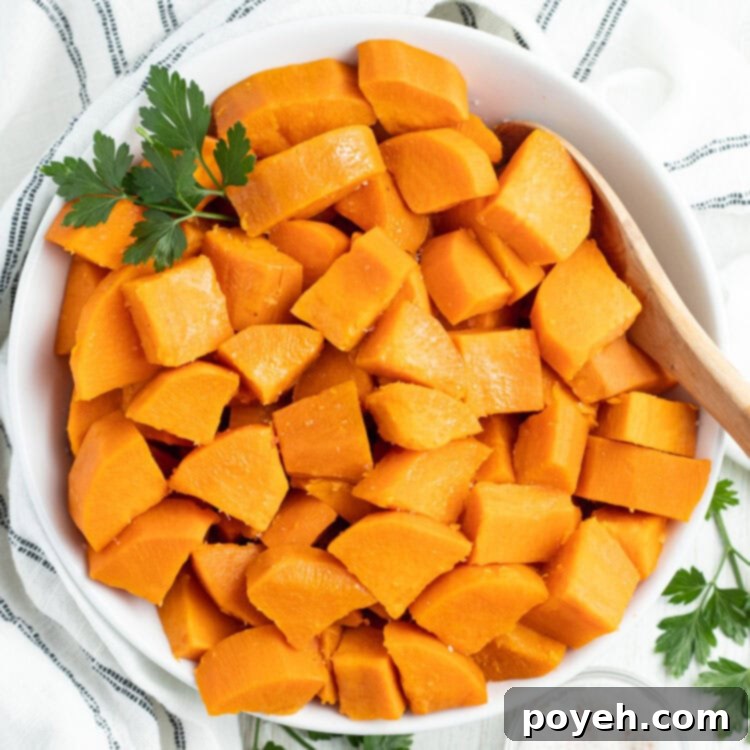 Overhead view of a large white bowl of cubed, boiled sweet potatoes on a table with a white tablecloth.