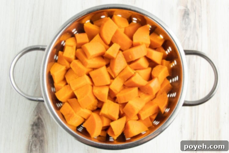 Overhead view of cubed sweet potatoes in a silver colander on a white table.