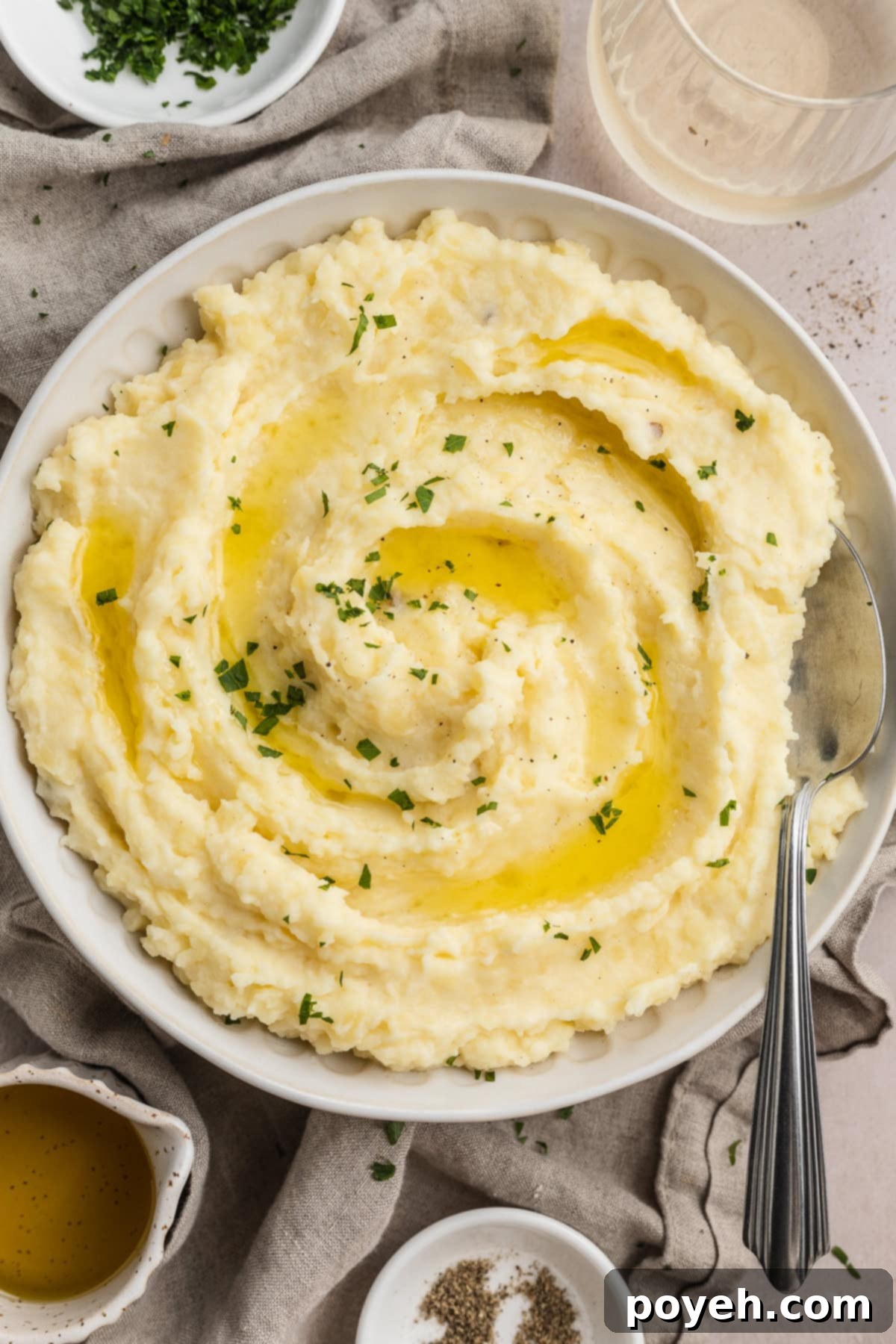 Overhead, zoomed out view of a large bowl of truffle mashed potatoes on a table set for the holidays, garnished with fresh herbs and a drizzle of truffle oil.
